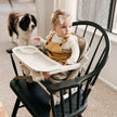 Baby sitting in a FeedMe Booster Seat, secure with harness and removable tray, on a dining chair, ideal feeding chair for toddlers.