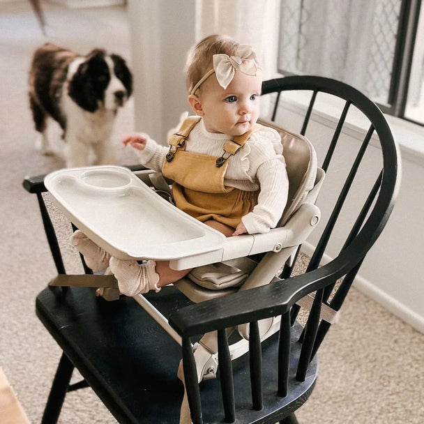 Baby sitting in a FeedMe Booster Seat, secure with harness and removable tray, on a dining chair, ideal feeding chair for toddlers.