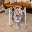 Baby enjoying Ingenuity Swing 'N' Go Portable Swing in Chambray with toy bar in cozy home setting.